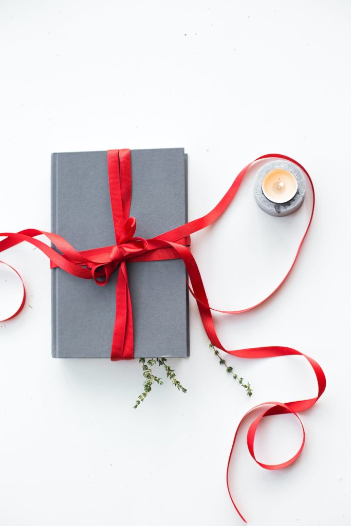 Grey notebook wraped with a red ribbon next to a tea light candle