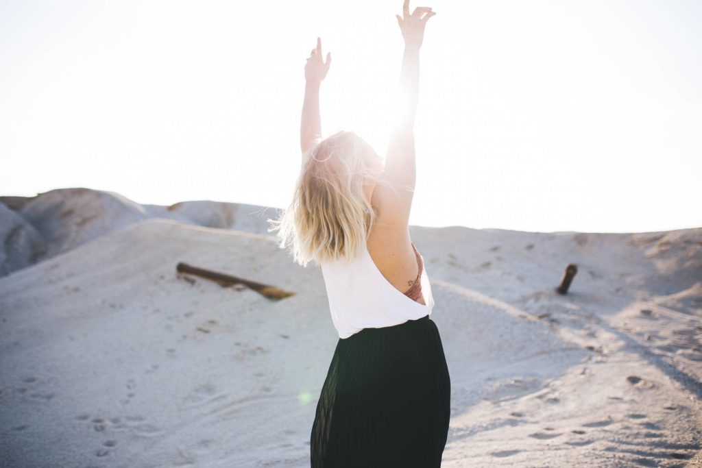 Women at the beach with sun shining through her upstretched arms