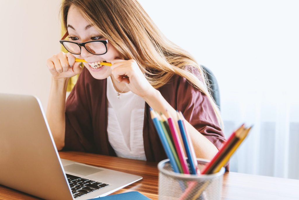 Woman biting a pencil while looking at a laptop