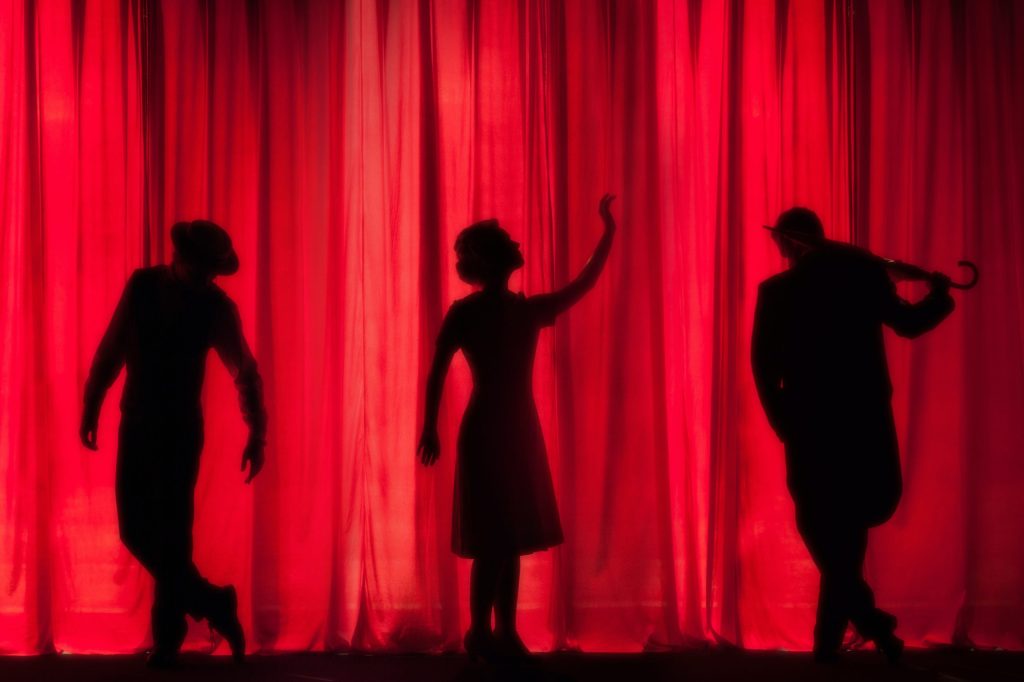 Silhouette of 3 actors on stage in front of a red curtain