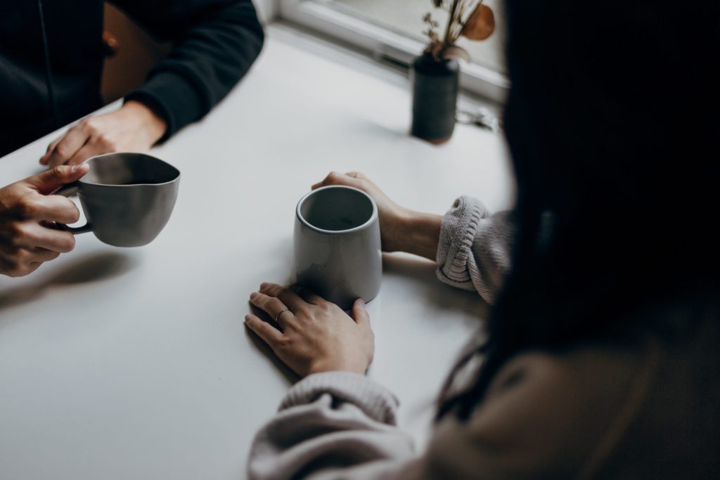 Close up picture of the hands of two people drinking out of mugs