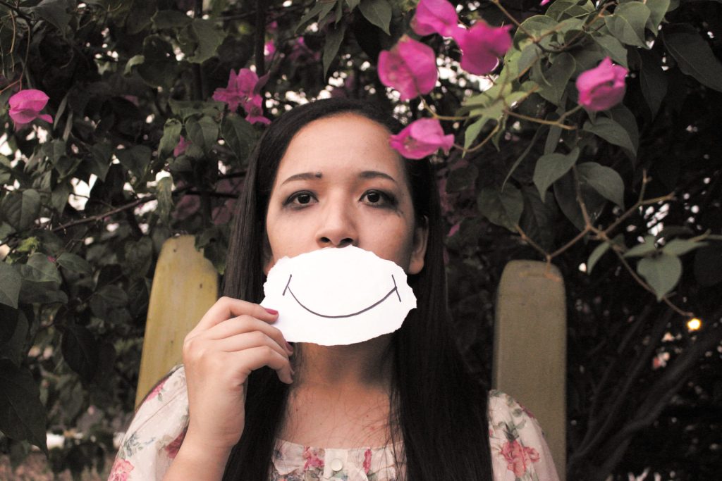 Woman who looks sad with the picture of a smile in front of her mouth