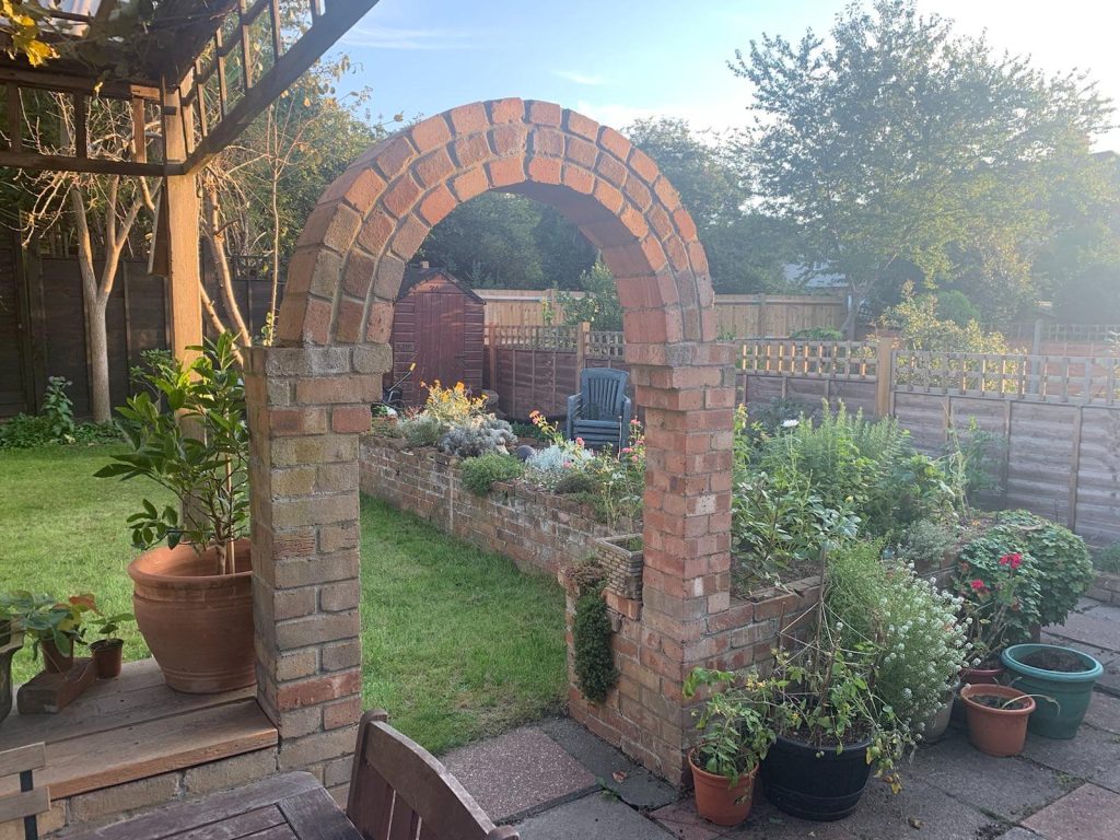 My garden on a sunny day. There is a brick arch and trhough it you can see the raised brick planter.