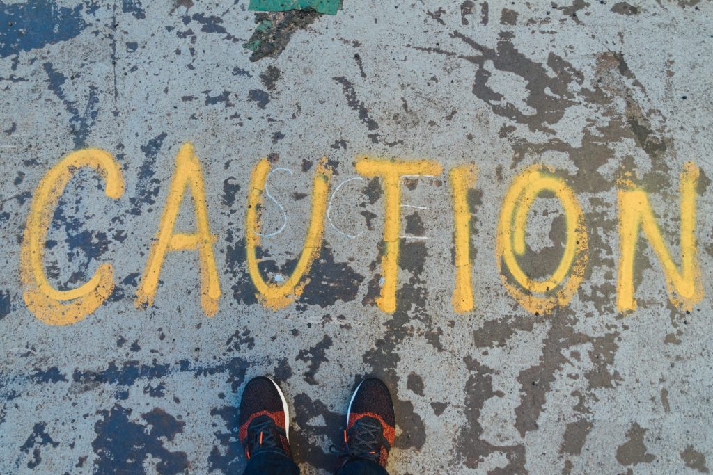 Caution written in yellow paint on the ground. You can see the shoes of the person standing in front of the word at the bottom of the image.