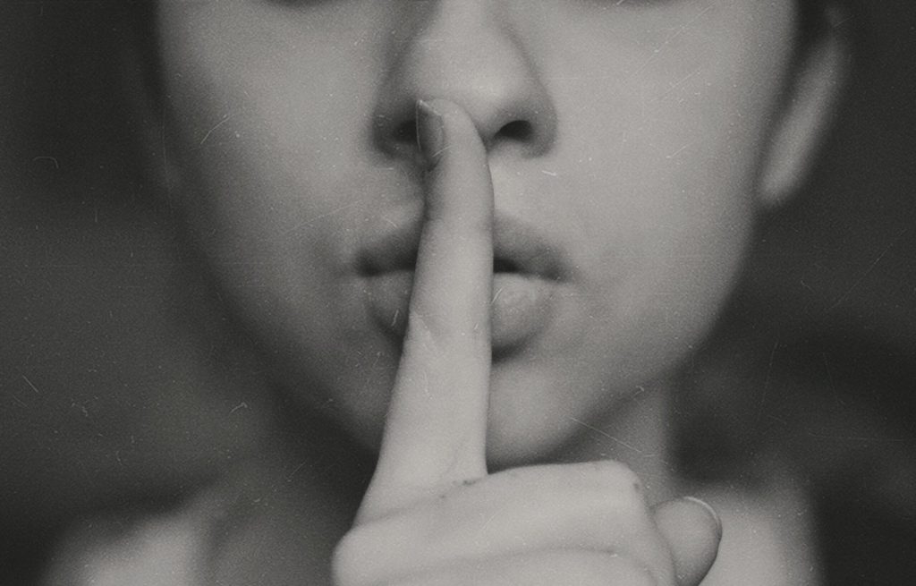 A close up of someone with their finger over their mouth to gesture silence.