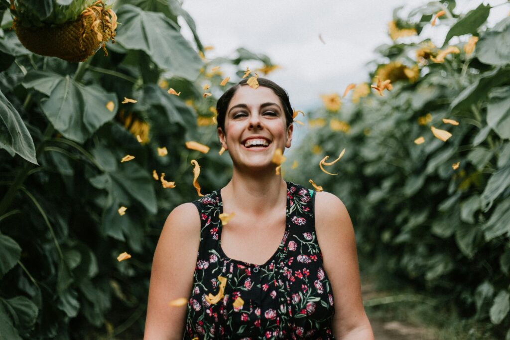 A women in a sunflower field. She is smiling as petals shower down on her. Photo by Priscilla Du Preez 🇨🇦 on Unsplash