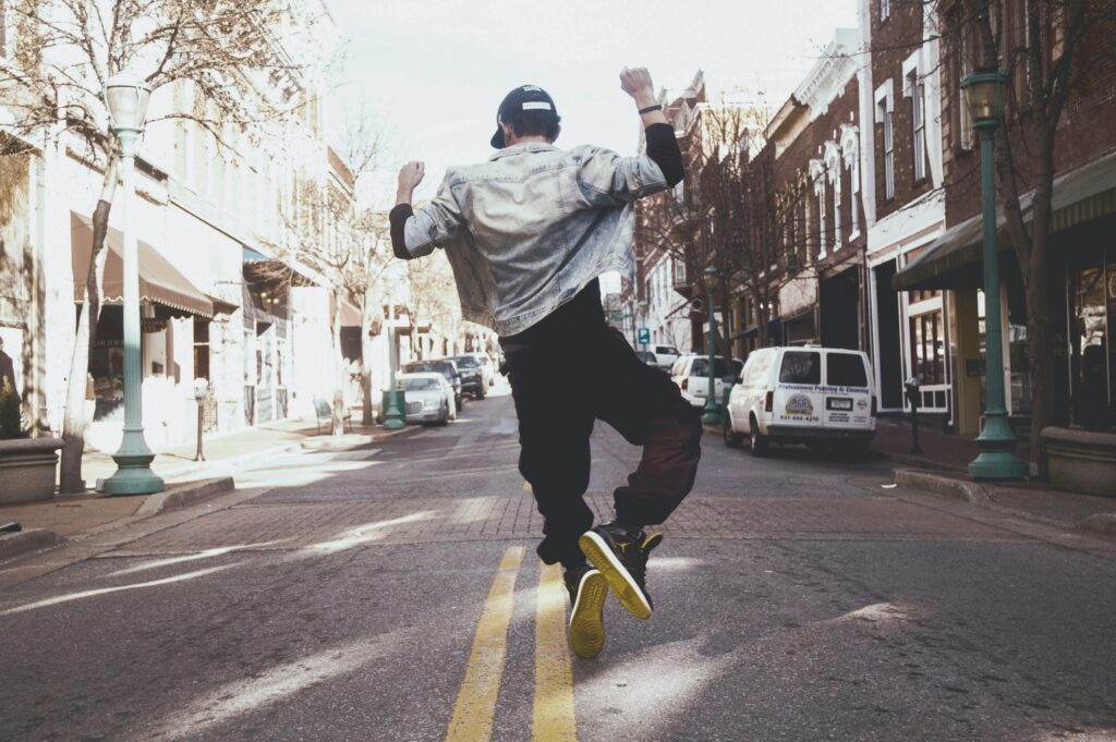 A person dancing down a quiet, car lined, street. Image credit: Photo by Andre Hunter on Unsplash