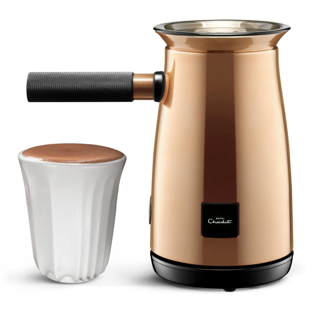 A bronze coloured Hotel Chocolate Velvetiser next to a white handless mug filled with hot chocolate.