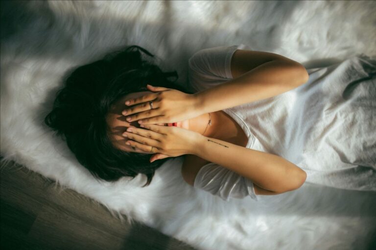 A person lying on a bed with their hands over their face. Photo credit: Anthony Tran on Unsplash